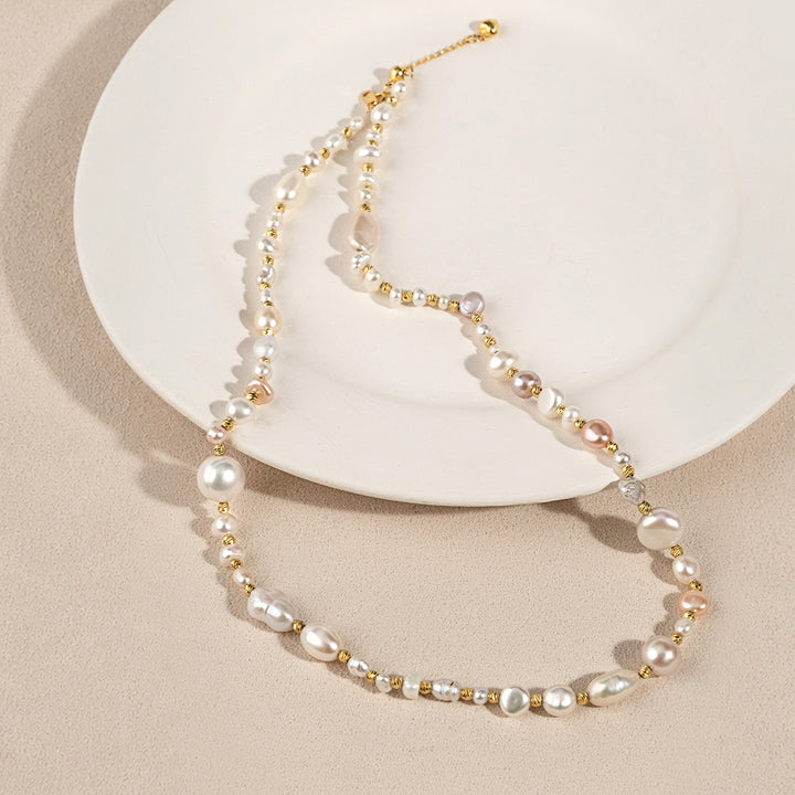 Baroque mixed freshwater pearl gold-plated necklace laid on white ceramic plate, detail view