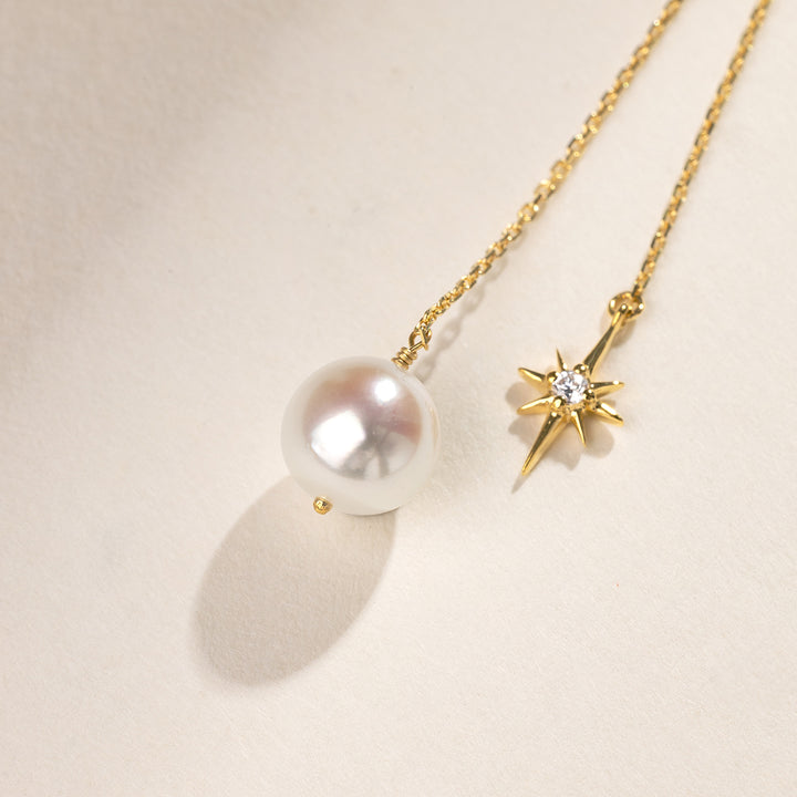 Detail flatlay of freshwater pearl and north star cubic zirconia charm on gold plating chain earring