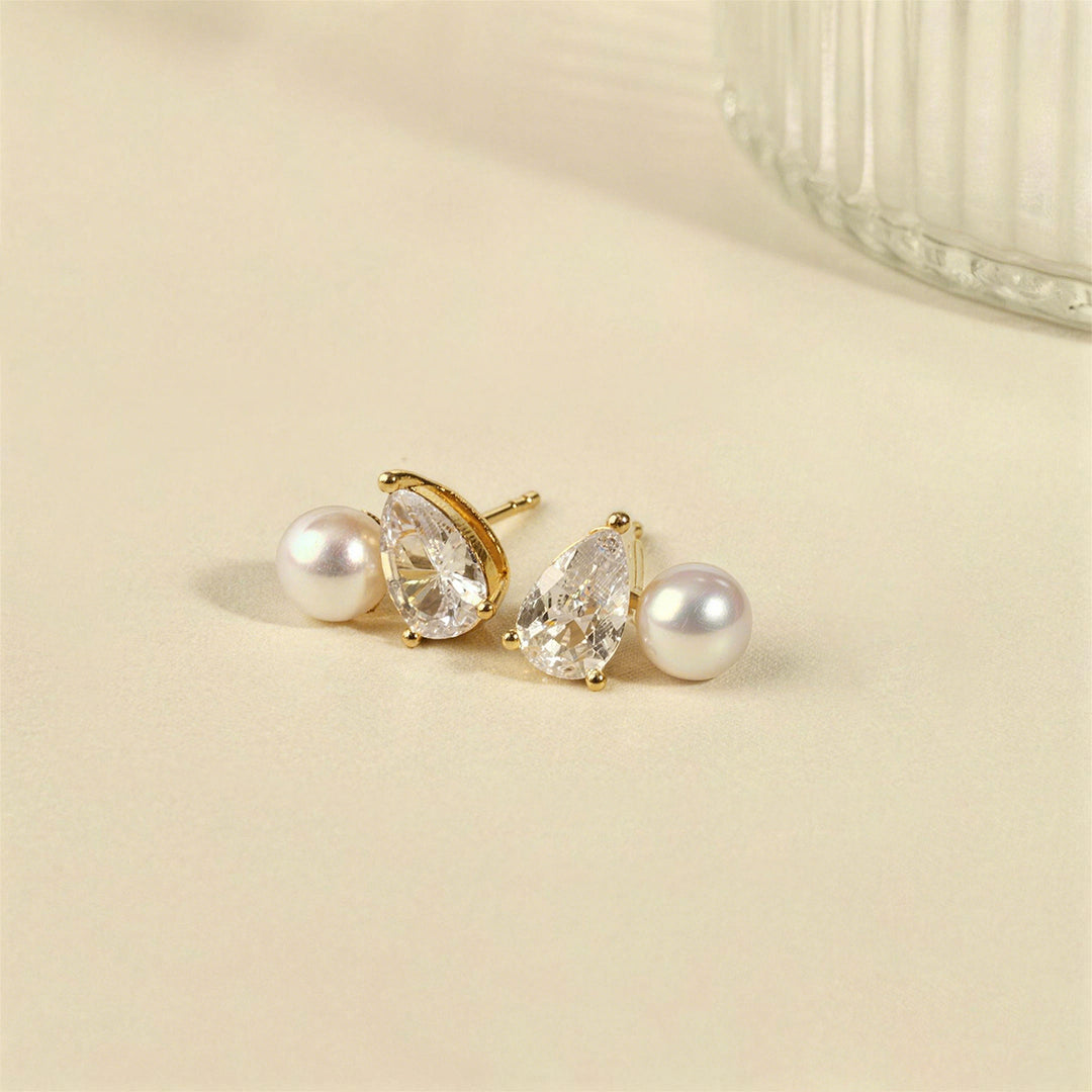 Gold plating freshwater pearl and pear-cut cubic zirconia stud earrings on cream surface, lifestyle flatlay