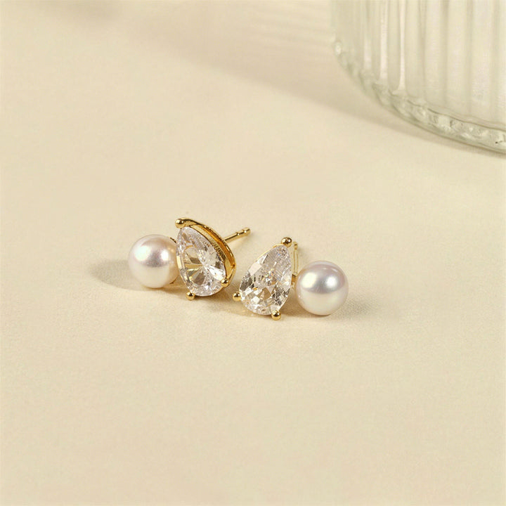 Gold plating freshwater pearl and pear-cut cubic zirconia stud earrings on cream surface, lifestyle flatlay