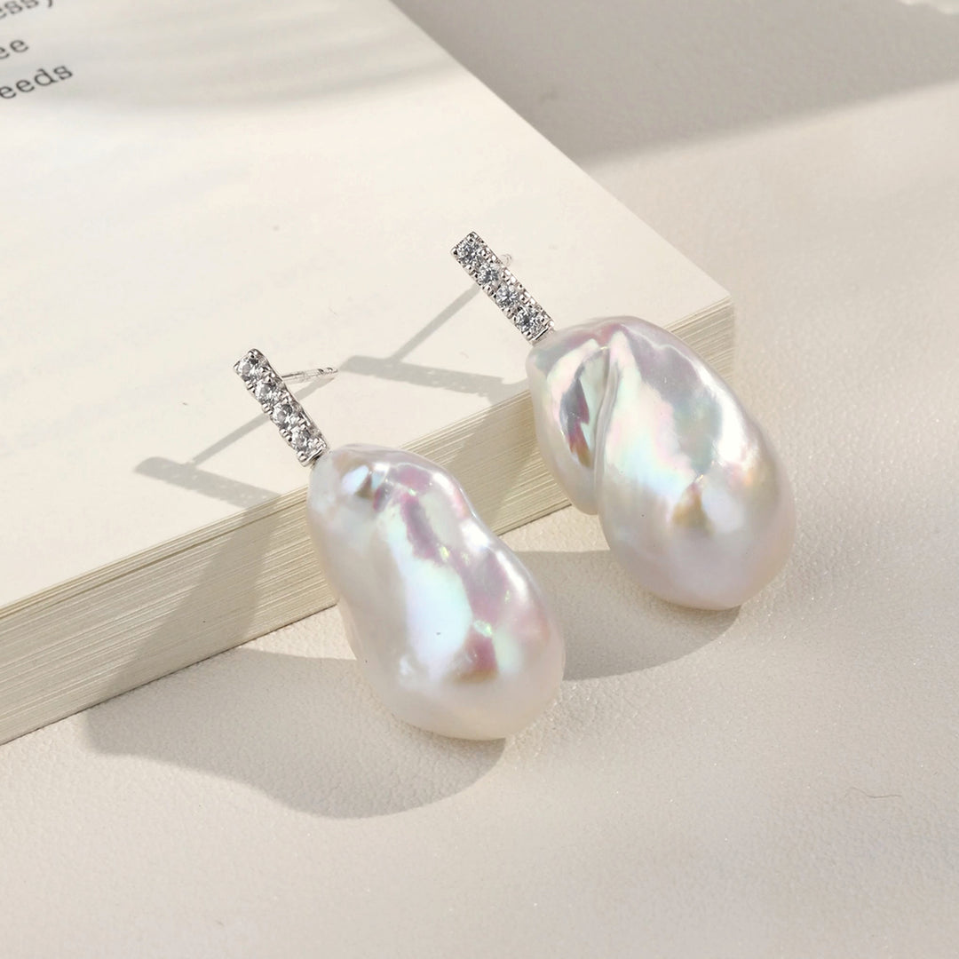 Baroque iridescent freshwater pearl CZ bar drop earrings on open book, showing pearl iridescence flatlay