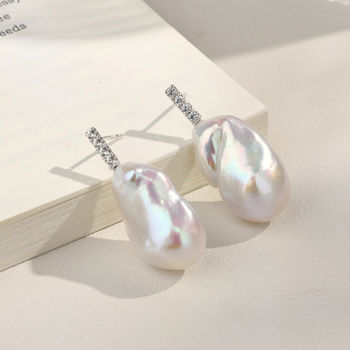 Baroque iridescent freshwater pearl CZ bar drop earrings on open book, showing pearl iridescence flatlay