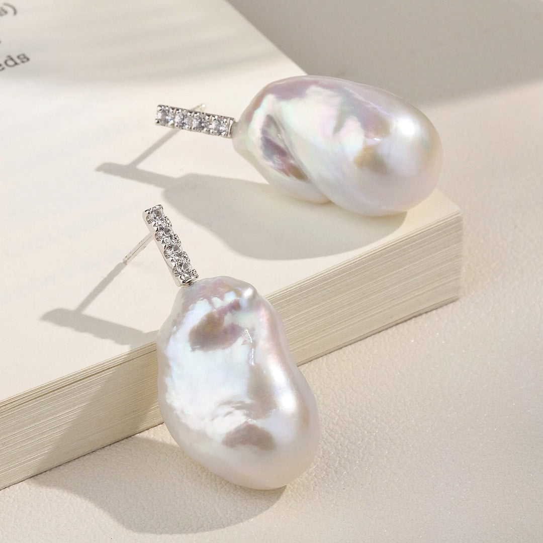 Detail flatlay of baroque iridescent freshwater pearl CZ bar drop earrings on book pages