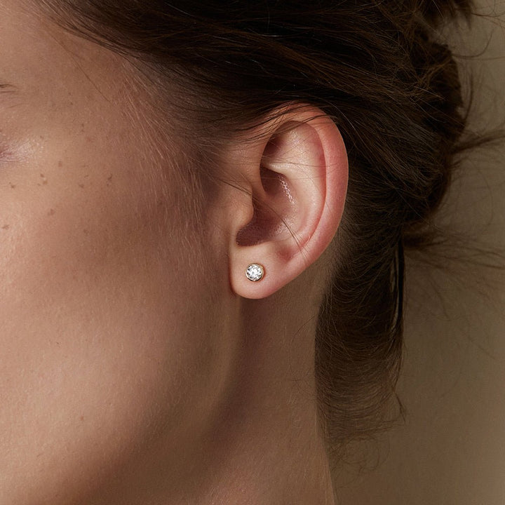 Model wearing lab-grown diamond gold vermeil bezel set round brilliant stud earring, close-up side view
