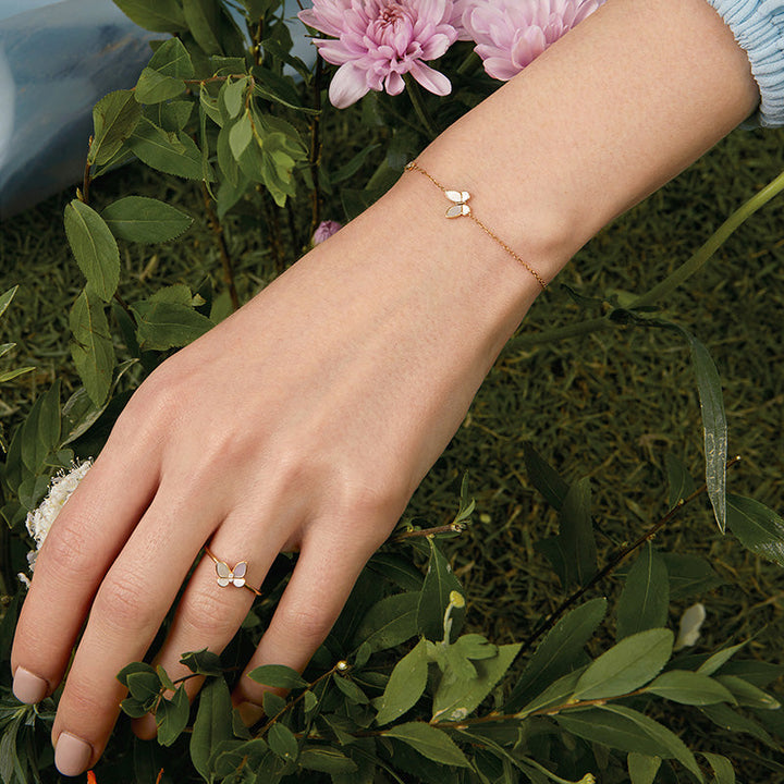 Model wearing mother-of-pearl gold vermeil butterfly bracelet and matching ring, styled with flowers and greenery