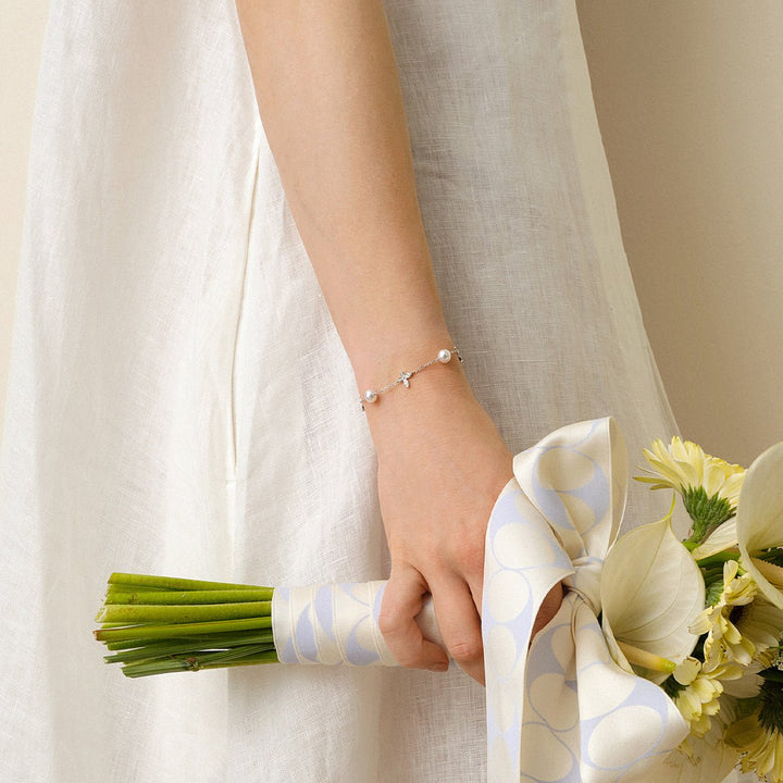 Model holding bridal bouquet wearing freshwater pearl lab-grown diamond butterfly bracelet in rhodium-plated sterling silver