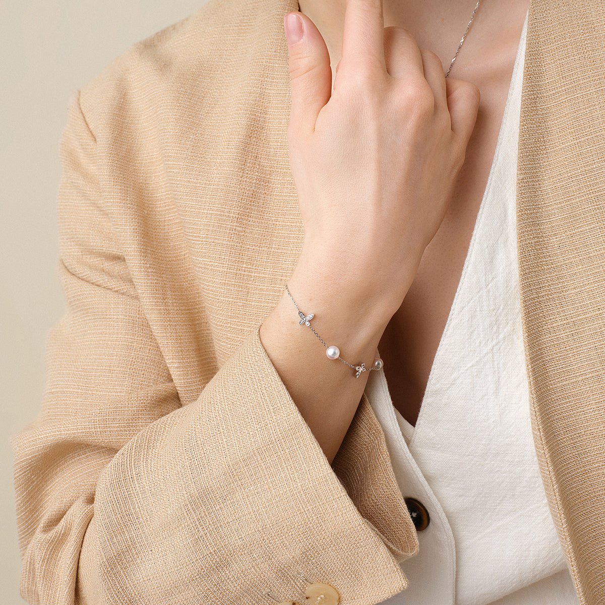 Model in beige blazer wearing freshwater pearl and diamond butterfly bracelet in 925 sterling silver
