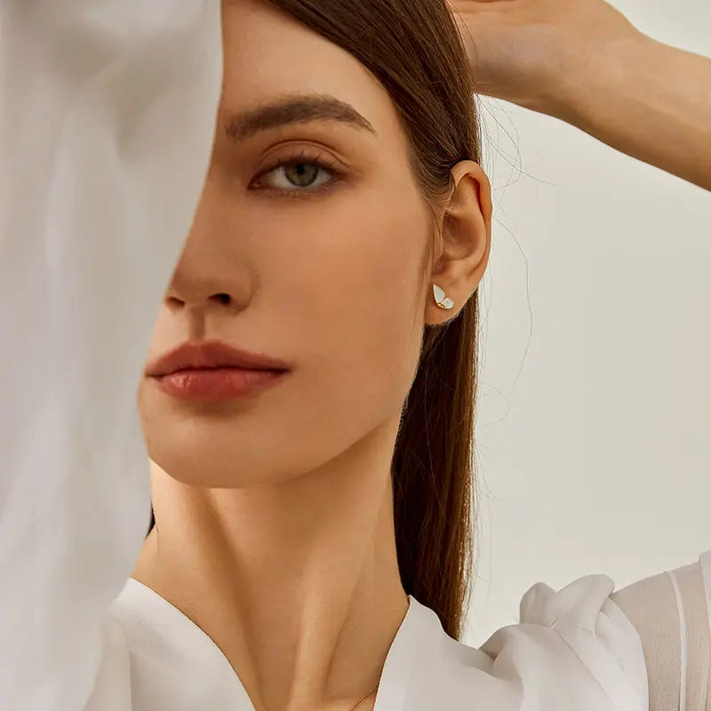 Model wearing mother-of-pearl gold vermeil butterfly stud earrings, styled with white top