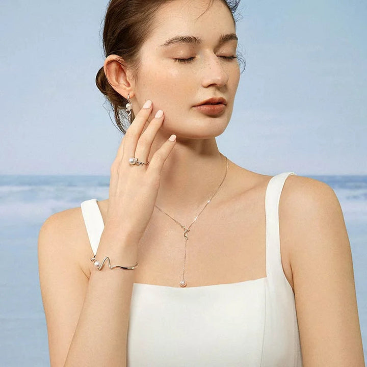 Model wearing freshwater pearl sterling silver diamond lariat necklace styled with bracelet and ring at beach